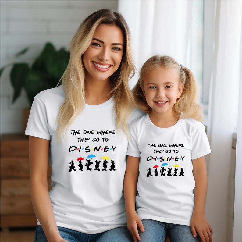 May include: White t-shirts for adults and children with the text "The one where they go to Disney" and a graphic of Mickey Mouse and friends walking with umbrellas.