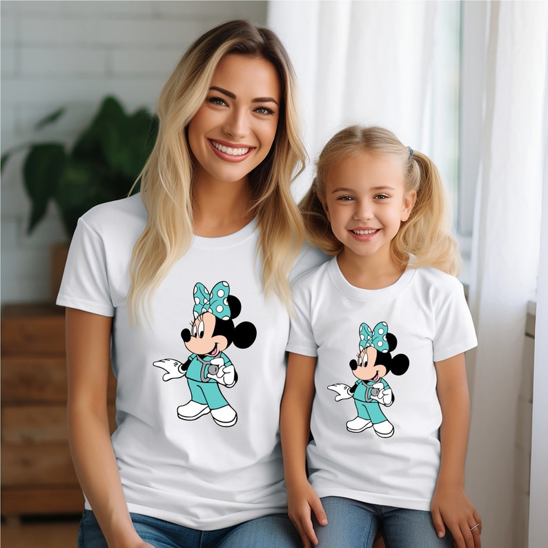May include: A white t-shirt with a cartoon image of Minnie Mouse dressed as a doctor. The shirt has a teal blue bow with white polka dots. The image is repeated on a smaller white t-shirt.