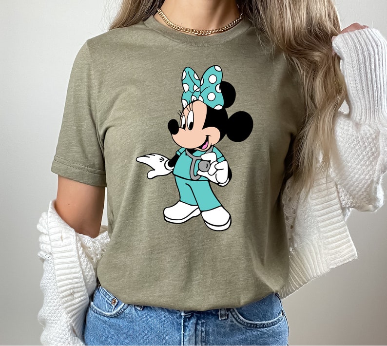 May include: A green t-shirt with a cartoon image of Minnie Mouse dressed as a nurse. Minnie is wearing a blue scrub top, a stethoscope, and a white bow with blue polka dots.