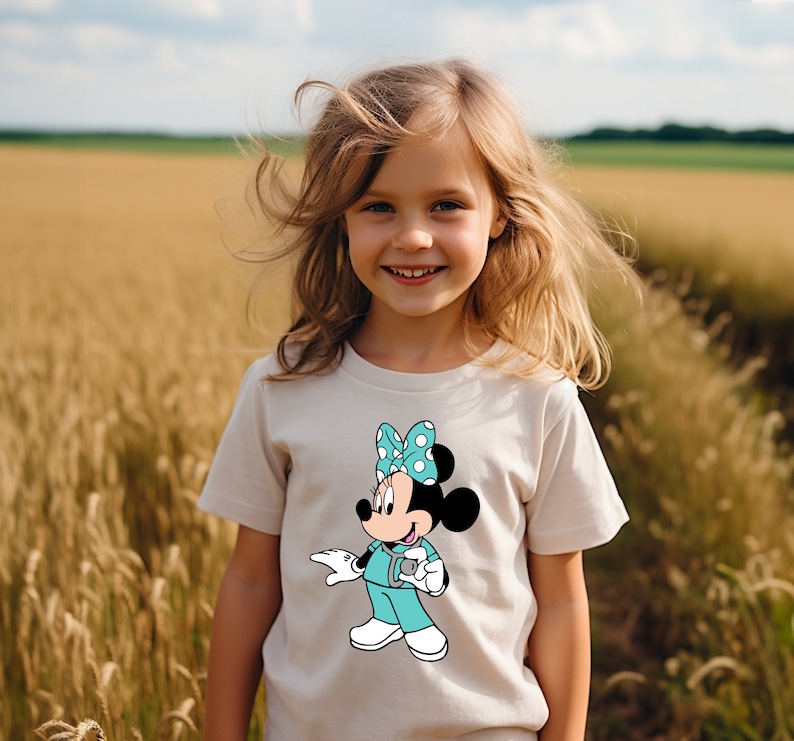 May include: A young girl wearing a white t-shirt with a cartoon image of Minnie Mouse dressed as a doctor. Minnie Mouse is wearing a turquoise scrub top with white polka dots and a white bow with blue polka dots. She is holding a stethoscope in her right hand.