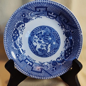 Peut inclure: Une assiette d&eacute;corative blanche et bleue avec un motif d&eacute;taill&eacute; de style Willow. L'assiette pr&eacute;sente une sc&egrave;ne centrale entour&eacute;e de bordures complexes et de motifs g&eacute;om&eacute;triques. L'assiette est pr&eacute;sent&eacute;e sur un support noir.