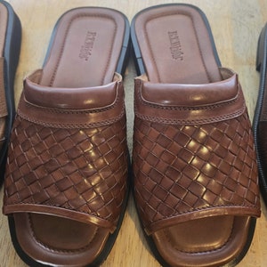 May include: A pair of brown leather woven slip-on sandals with a black sole. The sandals have a woven leather design and the brand name "BEVERLY" is embossed on the top of the sandals.
