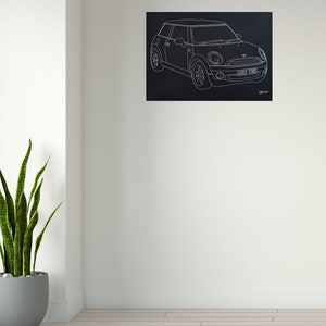 Puede incluir: Dibujo lineal blanco de un Mini Cooper sobre fondo negro. El coche se representa de perfil, mostrando sus caracter&iacute;sticas. La matr&iacute;cula dice "A162 CUB". La obra est&aacute; montada en una pared blanca.