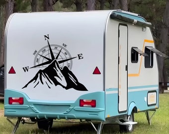 May include: A white and blue camper trailer with a compass and mountain graphic on the side. The compass has the directions N, NE, E, NW, W, and S.