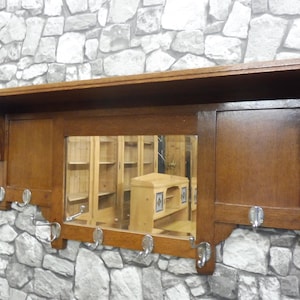 Puede incluir: Un perchero de pared de madera con un espejo y ganchos. El perchero está hecho de madera oscura y tiene un diseño simple. El espejo es rectangular y tiene un borde biselado. Los ganchos son de metal y están unidos a la parte inferior del perchero.