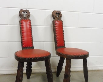 May include: Two antique wooden chairs with red leather seats and carved backs. The chairs have three legs each and are in good condition.