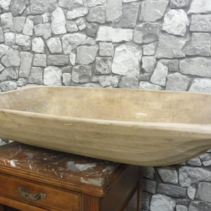 Op de afbeelding: Een grote, rechthoekige houten deegkom met een gladde, lichtbruine afwerking. De kom staat op een marmeren oppervlak.