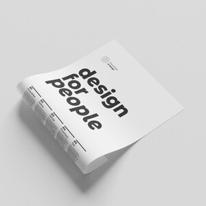 May include: A white sheet of paper with the text "design for people" printed in black bold letters. The paper is folded in half and the top edge is curled over.
