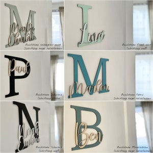 May include: A collection of wooden letter wall decor in various colors. Each letter has a name in a contrasting color. The letters are in shades of green, black, and blue. The names are in a cursive font.
