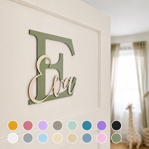 May include: A wooden wall decoration featuring the name "Eva" in a cursive font, layered over a large, green letter "E". The sign is mounted on a white door. A color palette of various hues is displayed below the sign.