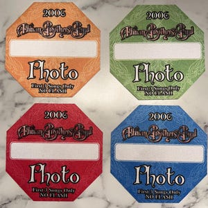 May include: Four octagonal Allman Brothers Band photo passes from 2006 in orange, green, red, and blue. Each pass features the band name, the year 2006, a white rectangular space for a name, and the text Photo First 3 Songs Only NO FLASH.