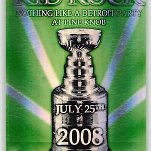 May include: A rectangular laminated pass featuring a green background with light rays. Text reads KID ROCK, NOTHING LIKE A DETROIT PARTY AT PINE KNOB, JULY 25TH 2008, and ALL ACCESS. A silver trophy cup graphic is centered on the pass.