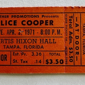 May include: An orange rectangular concert ticket for an Alice Cooper performance at Curtis Hixon Hall in Tampa, Florida, on Friday, April 2, 1971, at 8:00 P.M. The ticket features black text, the number 003044, and a total admission price of $3.50.