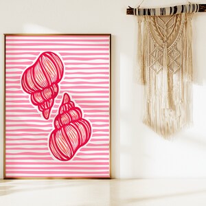 Op de afbeelding: Een ingelijst print met een roze en witte gestreepte achtergrond en twee rode schelpen. De schelpen zijn gestileerd en hebben een gedetailleerd lijntekenontwerp.