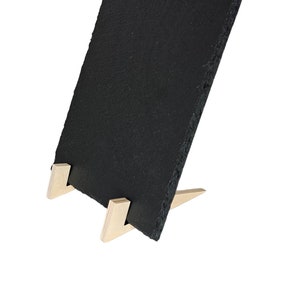 Pode incluir: Tabuleiro de servir de ardósia preta com um suporte de madeira. O tabuleiro é retangular e tem uma textura áspera e natural. O suporte é de madeira clara e tem forma triangular.