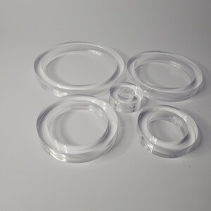 May include: A set of six clear acrylic circles of varying sizes. The circles are stacked on top of each other, with the largest circle at the bottom and the smallest circle at the top.