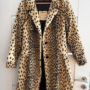 May include: A long-sleeved coat featuring a tan and black leopard print pattern. The coat has a notched collar, two black buttons on the front, and a black interior lining. A label inside the neck reads Safari by Fairmoor LaFrance.