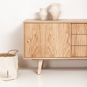 May include: A light wood cabinet with two doors and two drawers. The cabinet has a simple design with a light wood finish. Two white ceramic vases are on top of the cabinet.