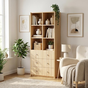 May include: A tall light wood bookcase featuring four open shelves filled with books, vases, and a woven basket, positioned above six drawers with small silver knobs. The unit has a vertical grain finish and provides organised storage space.