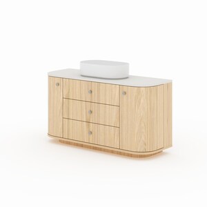 May include: A light wood vanity cabinet featuring a white countertop and an oval white vessel sink. The unit includes three central drawers and two side cabinets, all equipped with small, round, silver-toned knobs and curved edges.