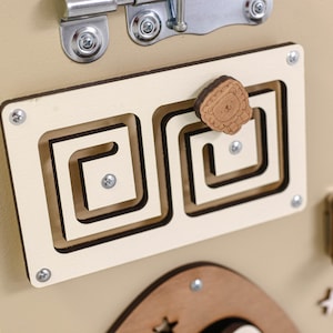 May include: A beige wooden activity board with a variety of textures and shapes for children to explore. The board features a small wooden lion with a brown mane, a latch, and a maze with a sliding piece.