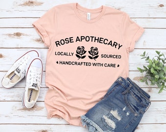 May include: A pink t-shirt with the text "ROSE APOTHECARY LOCALLY SOURCED HANDCRAFTED WITH CARE" and two black roses.