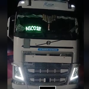 Peut inclure: Un camion Volvo blanc avec des phares lumineux et une calandre avant. Le texte "Mission" est au-dessus du pare-brise. Le texte lumineux "NIC018" est visible à l'avant du camion.
