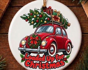 May include: A round white ceramic ornament featuring a red vintage car carrying a Christmas tree and wrapped gifts on its roof. The car has a wreath with a red bow on the front grille. The text Loaded Up for Christmas is printed in red.