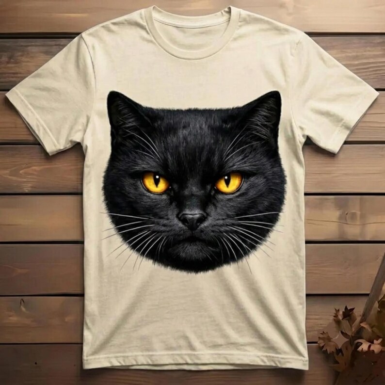 Detailed artwork of a mysterious black cat face with piercing orange eyes, designed as a bold aesthetic print for custom clothing and cat lovers.