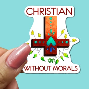 May include: A sticker with the words "CHRISTIAN WITHOUT MORALS" in a stylized font. The design features a cross with teal and blue accents, surrounded by green leaves and vines. The sticker is held against a light blue background.