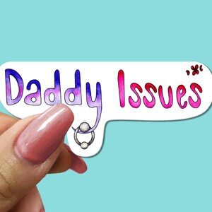 May include: A white sticker with the words "Daddy Issues" in a colorful, bubble-style font. The word "Daddy" is in purple and blue, and "Issues" is in pink. A small silver piercing is attached to the word "Daddy".