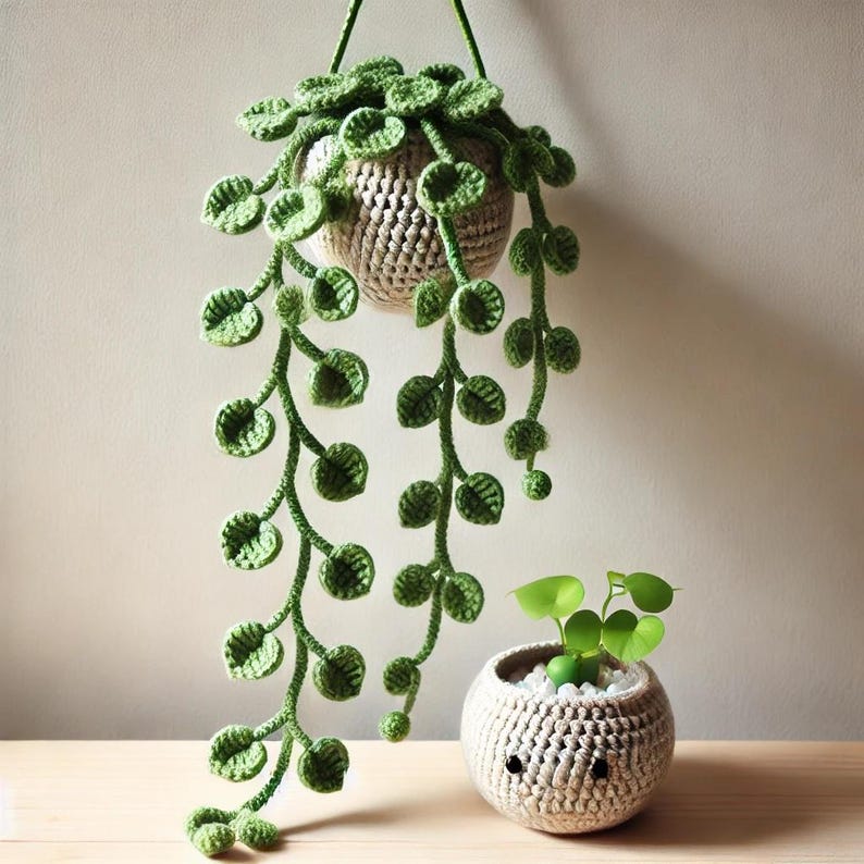 May include: Two crocheted hanging planters with green leaves. The larger planter is hanging from the ceiling and the smaller planter is sitting on a wooden surface.