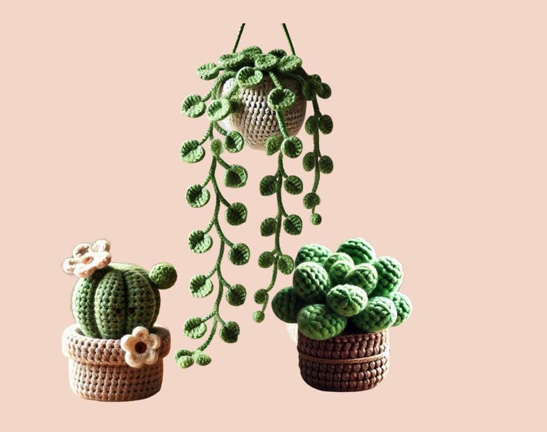 May include: Three crocheted potted plants. A green cactus with white flowers in a brown pot, a green succulent in a brown pot, and a hanging green plant with a brown pot.