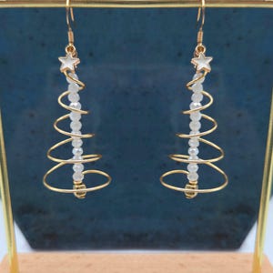 May include: Gold-colored spiral earrings with a Christmas tree design. Each earring features a white star at the top and a strand of white beads. The spiral design is made of gold-colored wire.