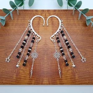 May include: A pair of silver ear cuffs with dangling chains and black beads. The chains feature small silver stars and a silver mandala charm.