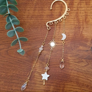 May include: Gold ear cuff with dangling charms, including a star, sun, moon, and crystal beads.