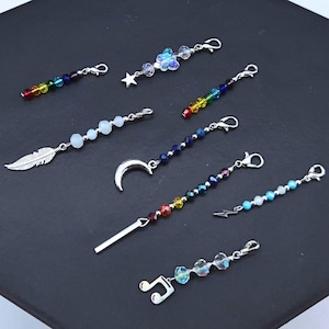 May include: A selection of beaded charms with silver clasps. Designs include rainbow beads, a butterfly, a star, a feather, a crescent moon, a lightning bolt, a bar, and a musical note. The charms are presented on a dark background.