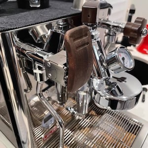 Pode incluir: Close-up de uma m&aacute;quina de caf&eacute; expresso profissional com acabamento cromado polido. Apresenta uma pega de madeira, um man&oacute;metro e uma bandeja de gotejamento em a&ccedil;o inoxid&aacute;vel. A m&aacute;quina tem um design elegante e moderno, ideal para uso dom&eacute;stico ou comercial.