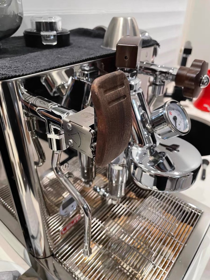 Pode incluir: Close-up de uma m&aacute;quina de caf&eacute; expresso profissional com acabamento cromado polido. Apresenta uma pega de madeira, um man&oacute;metro e uma bandeja de gotejamento em a&ccedil;o inoxid&aacute;vel. A m&aacute;quina tem um design elegante e moderno, ideal para uso dom&eacute;stico ou comercial.