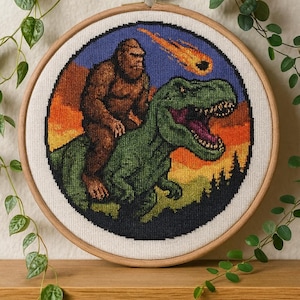 May include: Cross-stitch hoop art featuring a brown Bigfoot riding a green Tyrannosaurus Rex, with a fiery meteor in the sky. The background transitions from orange to blue. The artwork is framed in a wooden hoop.