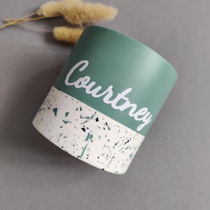 May include: A green and white terrazzo planter with the name "Courtney" written in white on the green portion.