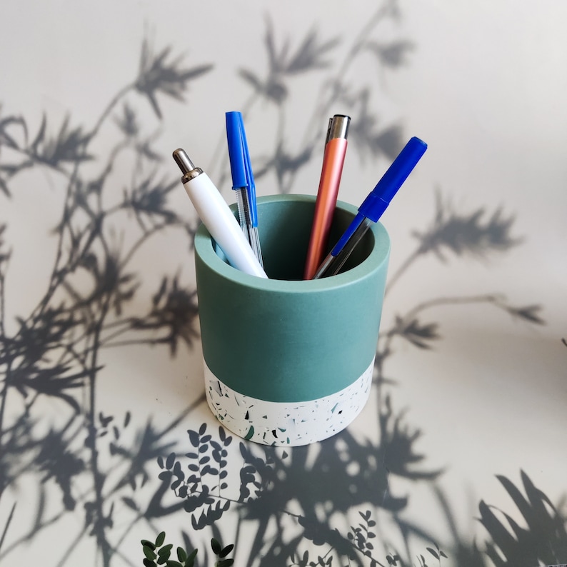 A green and white jesmonite pencil holder with four pens inside. Two of the pens are blue, one pink and one is white.