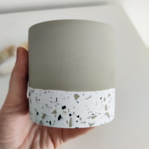May include: A small, light green planter with a white and black speckled terrazzo design around the bottom edge.