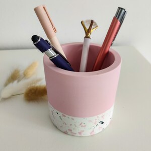 Pink and white terrazzo pencil holder with four pens inside. The holder is cylindrical and has a pink top and a white terrazzo bottom.