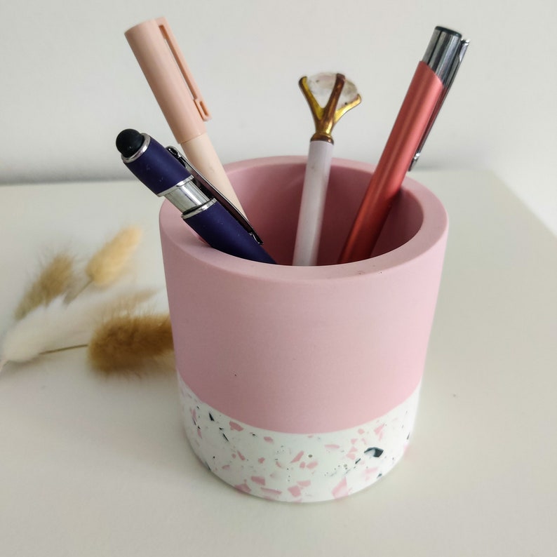 Pink and white terrazzo pencil holder with four pens inside. The holder is cylindrical and has a pink top and a white terrazzo bottom.