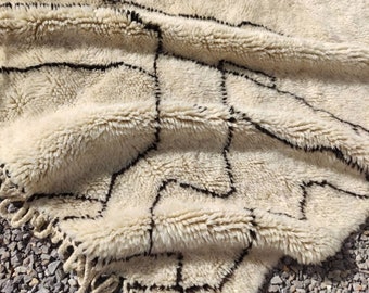 Könnte beinhalten: Ein weißer und schwarzer marokkanischer Teppich mit geometrischem Muster. Der Teppich ist aus Wolle und hat eine weiche, flauschige Textur.