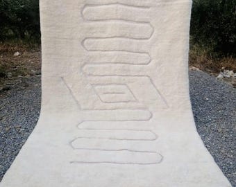 May include: White wool rug with a geometric pattern woven into the fabric. The rug has a fringe border.