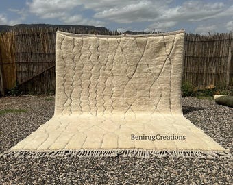 May include: A large, cream-colored rug with a geometric pattern and fringe detail. The rug is displayed outdoors against a backdrop of a wooden fence and a cloudy sky. The text "BenirugCreations" is visible on the rug.