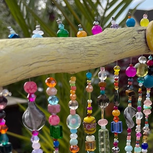 Pode incluir: Um m&oacute;bile de contas coloridas pendurado em um galho desgastado. As contas s&atilde;o feitas de vidro, madeira e outros materiais e s&atilde;o enfiadas em arame. O m&oacute;bile &eacute; uma pe&ccedil;a de arte linda e &uacute;nica que adicionaria um toque de fantasia a qualquer casa.