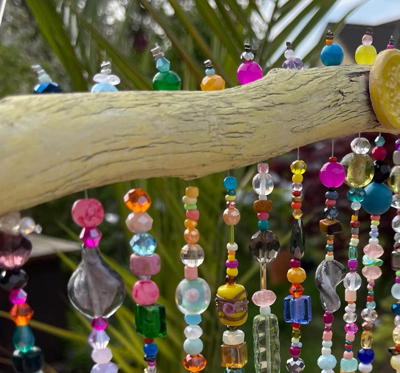 Pode incluir: Um m&oacute;bile de contas coloridas pendurado em um galho desgastado. As contas s&atilde;o feitas de vidro, madeira e outros materiais e s&atilde;o enfiadas em arame. O m&oacute;bile &eacute; uma pe&ccedil;a de arte linda e &uacute;nica que adicionaria um toque de fantasia a qualquer casa.